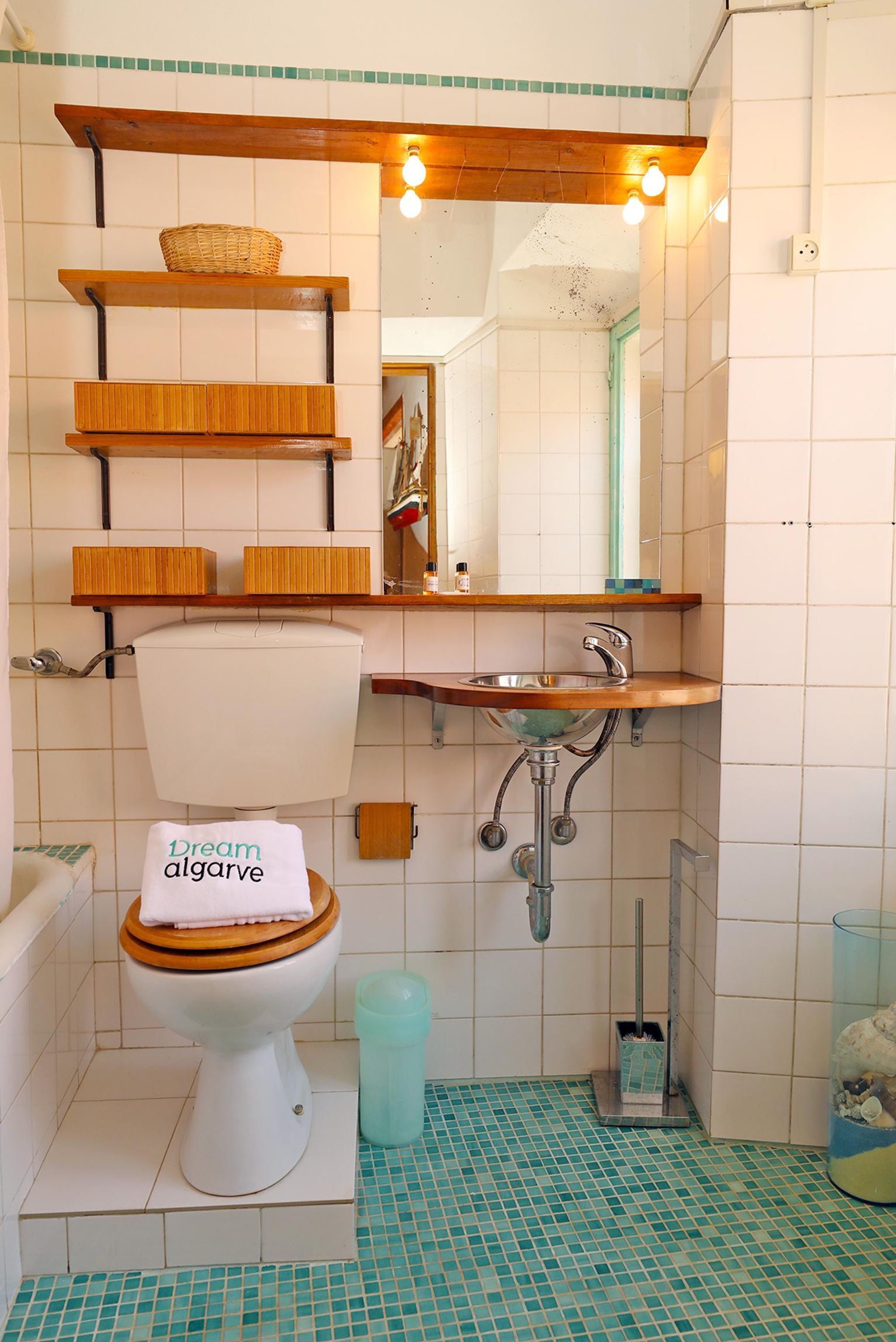 Une salle de bain avec des toilettes, un lavabo et une douche. Il y a des étagères au-dessus des toilettes et un miroir au-dessus du lavabo.