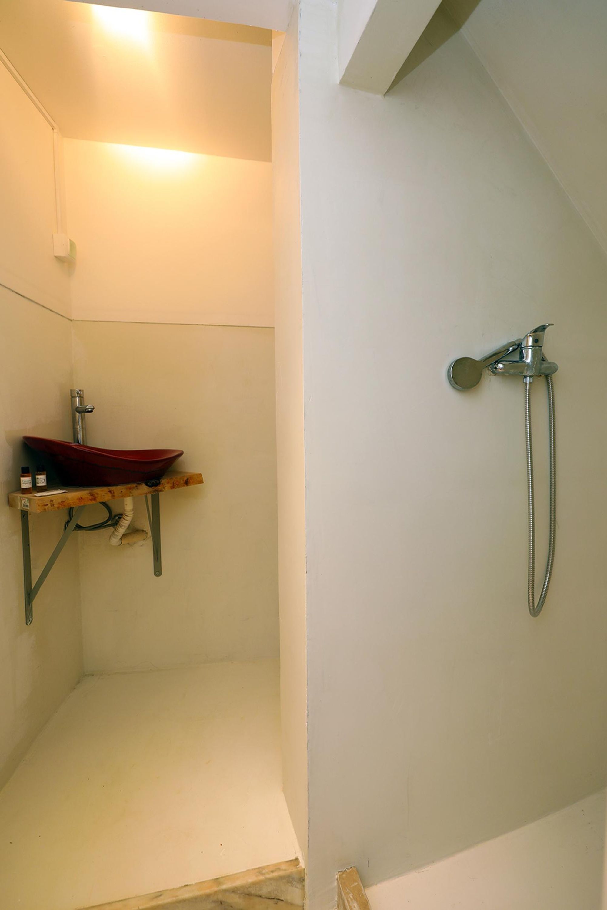 A bathroom with a red vessel sink, a shower with a handheld showerhead, and a white wall.