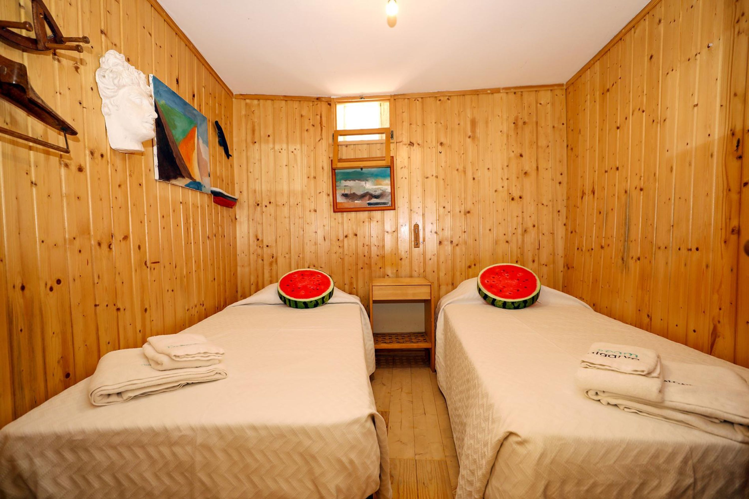 A room with wooden panel walls, two beds with towels, a small table, and a painting.