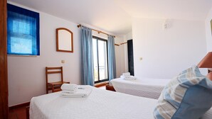 A hotel room with two beds, a window with curtains, a wooden chair, and a wall-mounted mirror. - B46 - Belavista Torraltinha Flat (Lagos)