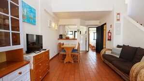 A living room with a TV, wooden furniture, a dining area, and a sofa. - B46 - Belavista Torraltinha Flat (Lagos)
