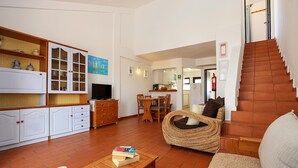 A spacious living room with a wooden coffee table, a wicker sofa, and a dining area with wooden chairs and a table. - B46 - Belavista Torraltinha Flat (Lagos)