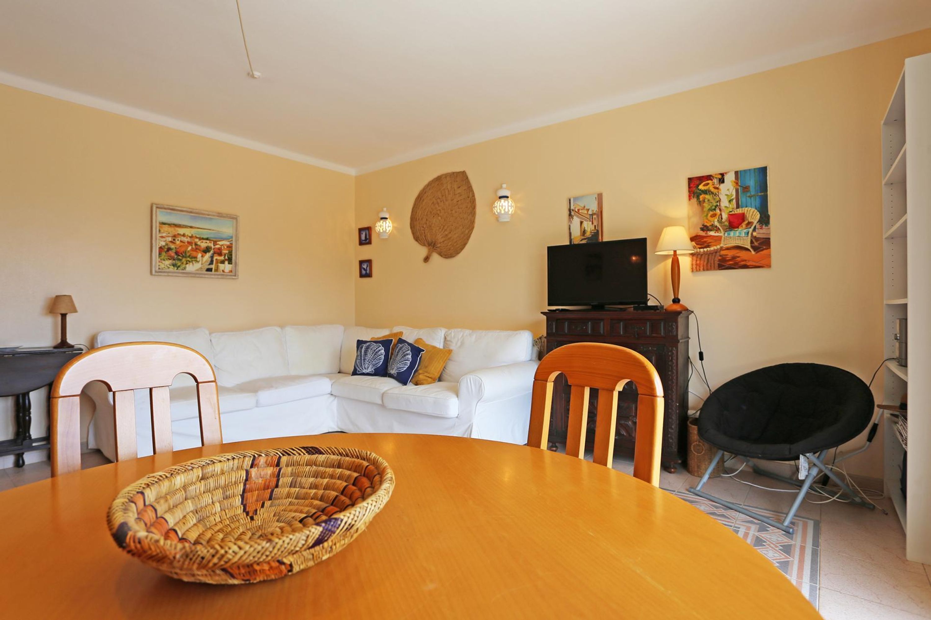 A living room with a white sofa, a wooden dining table, and a TV.