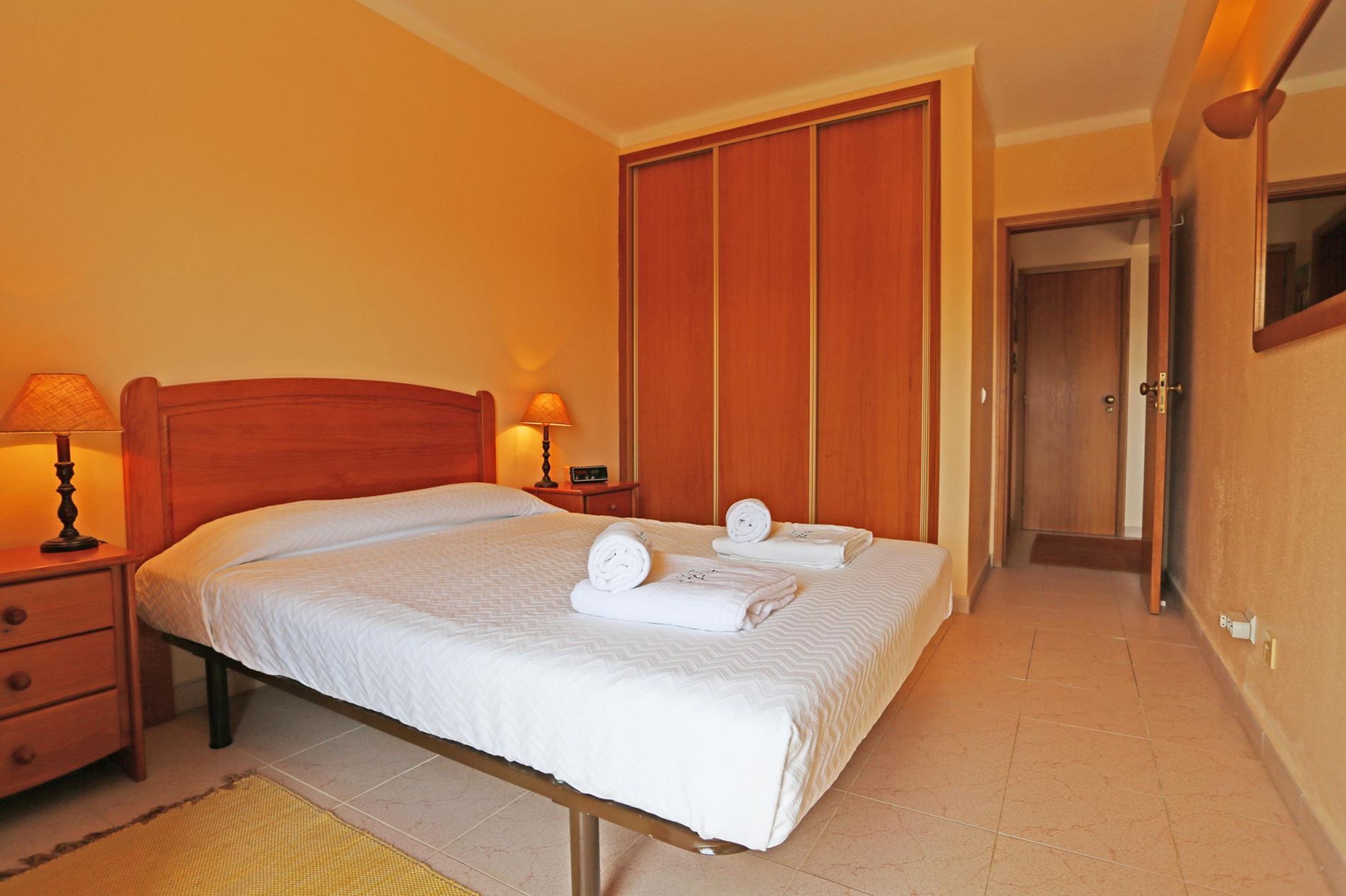 A hotel room with a bed, two bedside tables with lamps, a wardrobe, and a door leading to another room.