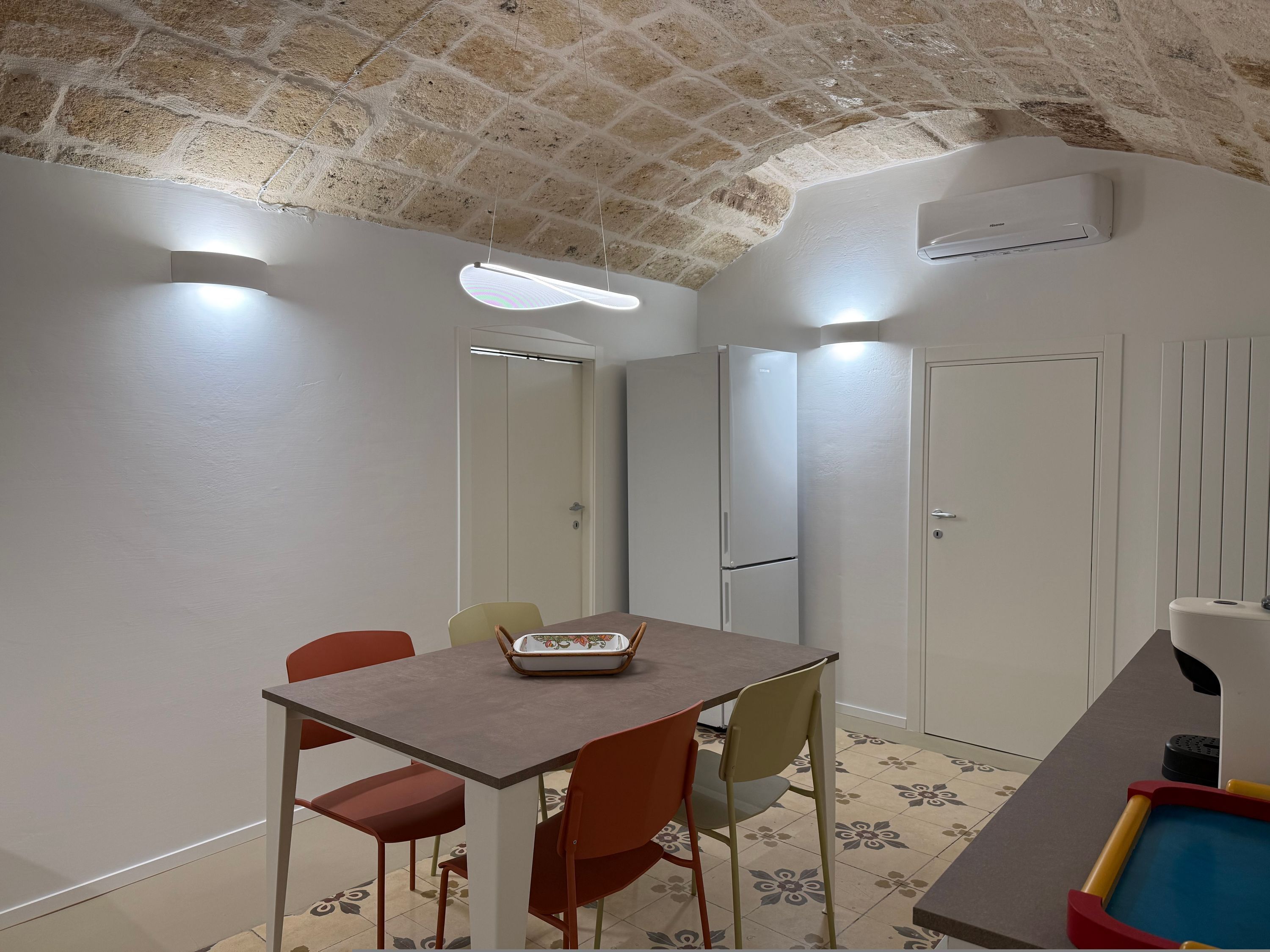Ein Zimmer mit Ziegeldecke, weißen Wänden, einem Tisch mit Stühlen, einem kleinen Tisch mit einem Korb und einer Toilette.