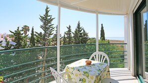 Un balcón con mesa y sillas, con vistas a un paisaje costero con árboles y edificios.