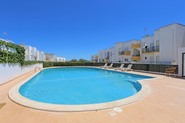 Una piscina con sillones de descanso y un cielo azul despejado.