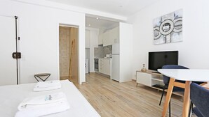 A modern hotel room with a bed, a desk with a chair, a television, and a kitchen area visible through an open door. - A09 - Sidestreet Mineiro Studio (Lagos)