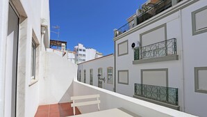 A narrow urban street with white buildings, a tiled patio, and a white bench. - A09 - Sidestreet Mineiro Studio (Lagos)