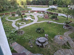 Ein gepflegter Garten mit einem runden Steintisch, einer Holzbank und einem kleinen Pavillon.