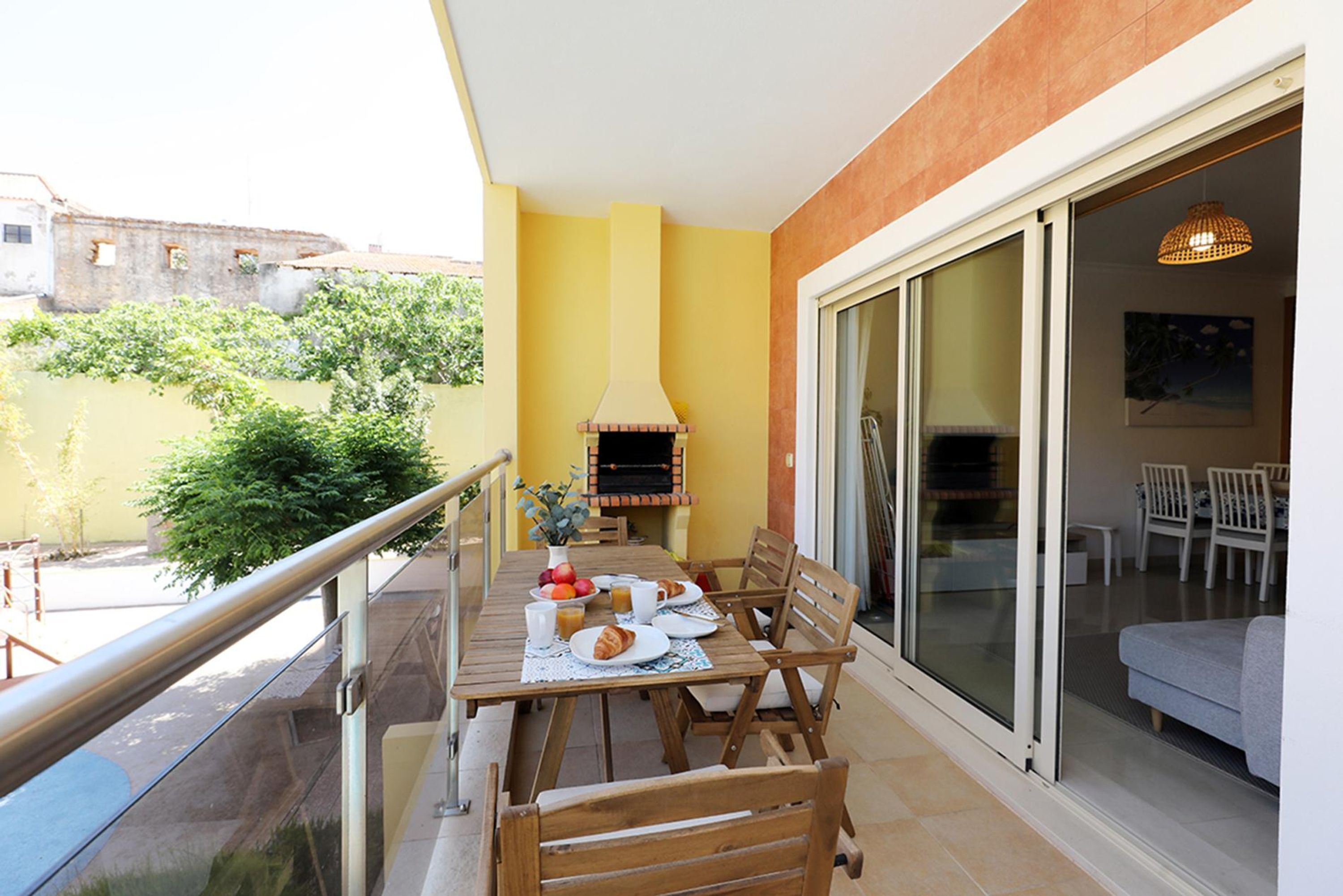A balcony with a table set for breakfast, a grill, and a sliding glass door leading to an indoor area.