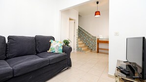 Una sala de estar con un sofá negro, un televisor y una escalera al fondo.