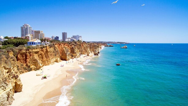 A coastal beach with clear blue waters, sandy shores, and rocky cliffs.