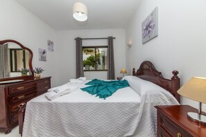 A hotel room with a bed, a dresser, a mirror, a window with curtains, a lamp, and wall art. - D02 - Carrob Street House (Lagos)
