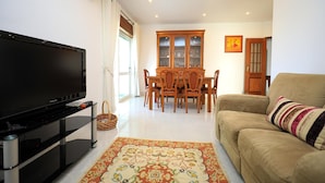 A living room with a flat-screen TV, a beige sofa, a dining table with chairs, and a patterned rug. - C23 - Parkway Entrance Apartment in Lagos (Lagos)