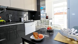A modern kitchen with a black countertop, white cabinets, and a dining area with a table set for two. - C23 - Parkway Entrance Apartment in Lagos (Lagos)