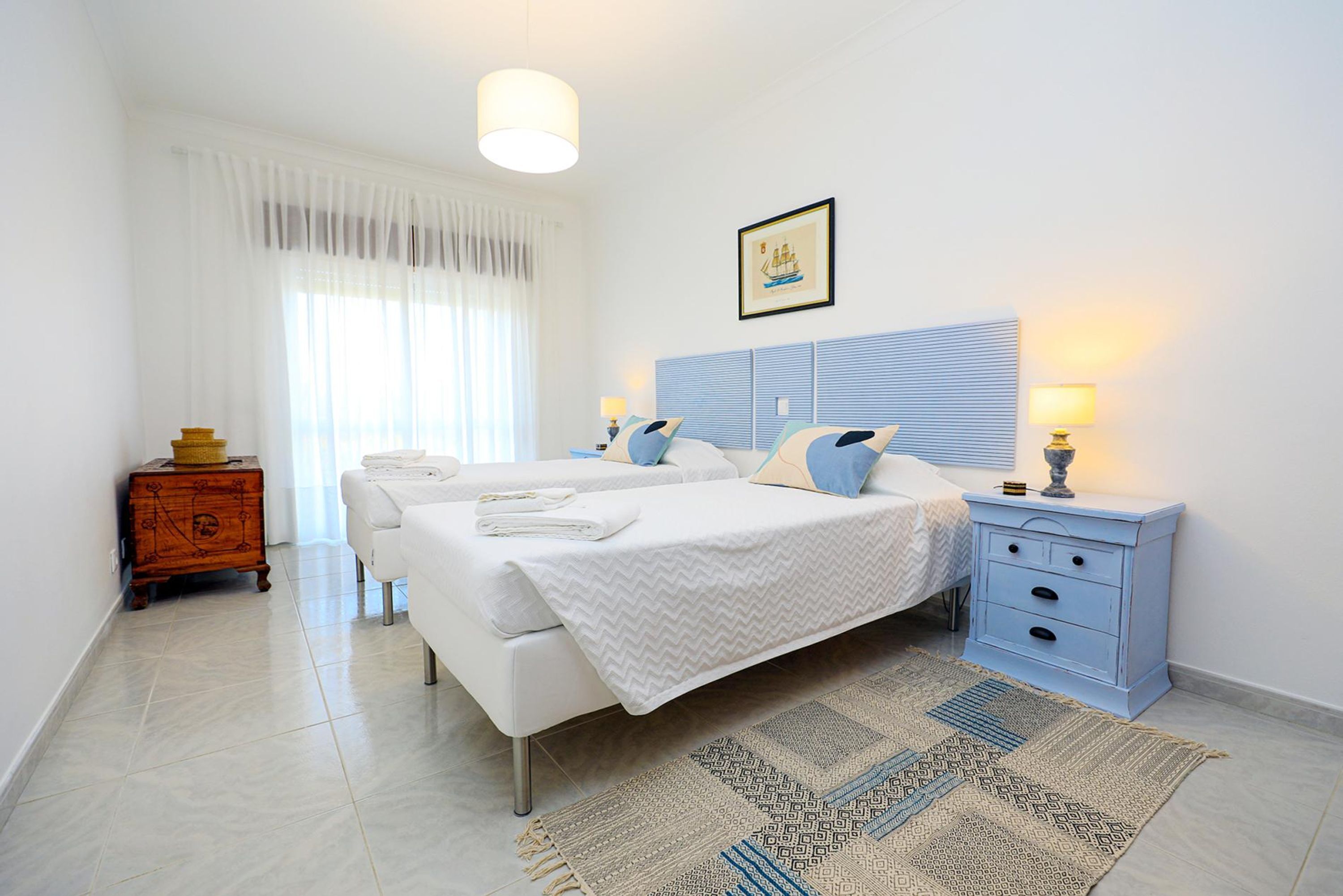 A bedroom with a bed, bedside tables, a nightstand, a dresser, and a window with curtains.