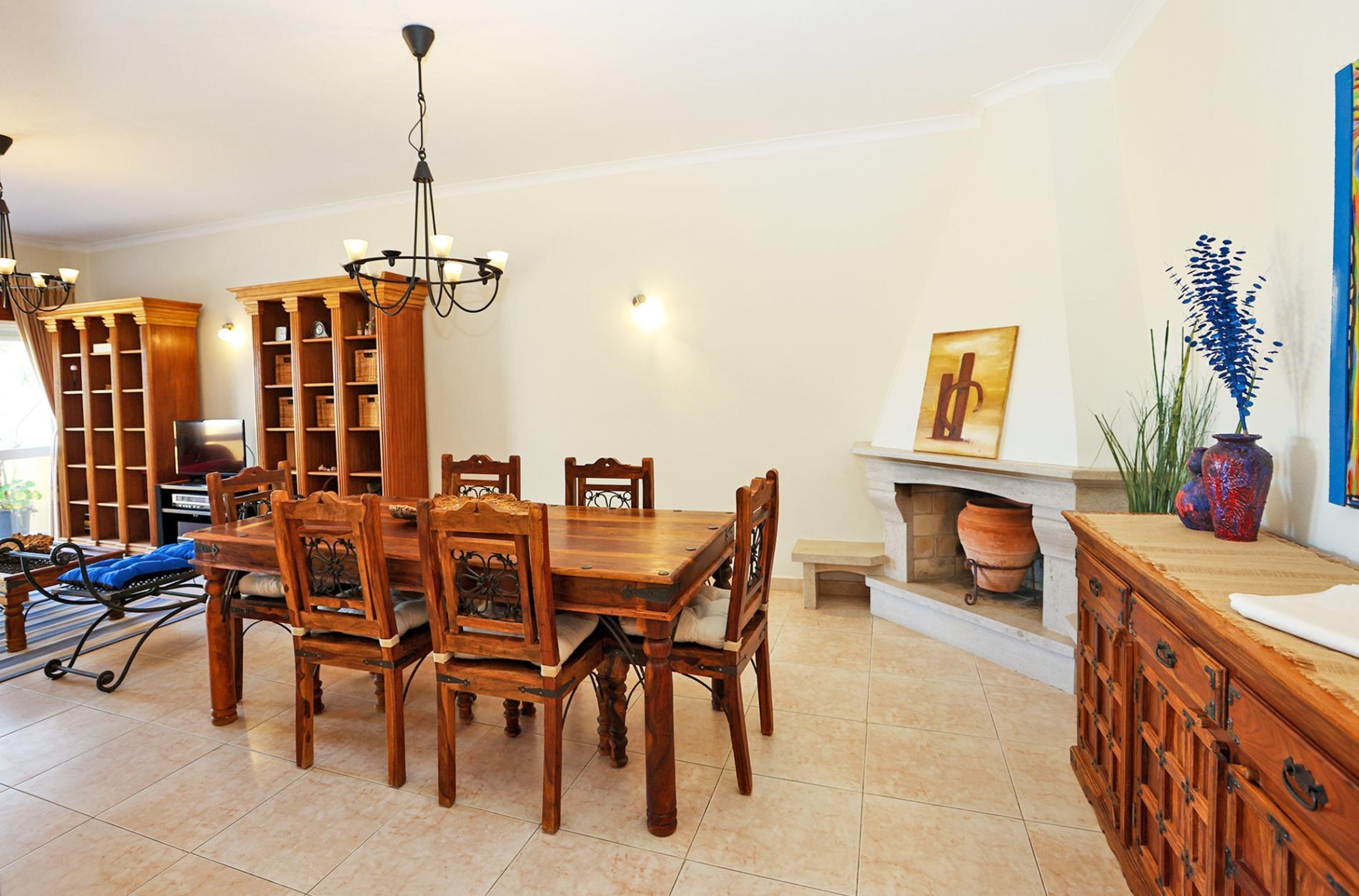A dining area with a wooden table and chairs, a chandelier, and a fireplace.