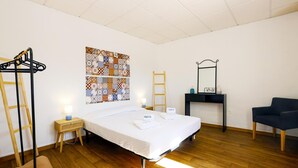 Ein Hotelzimmer mit einem Bett, Holzboden, Wandregal, Schreibtisch mit Spiegel und einem Stuhl.
