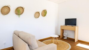 Ein minimalistisches Wohnzimmer mit einer Couch, einem kleinen runden Tisch, einem Fernseher auf einem Holzboden und einer Wandkorb mit Grünpflanzen.