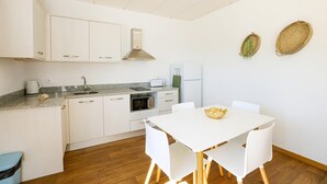 Eine moderne Küche mit weißen Schränken, einer Granitarbeitsplatte, einem eingebauten Ofen und einem weißen Esstisch mit vier Stühlen.