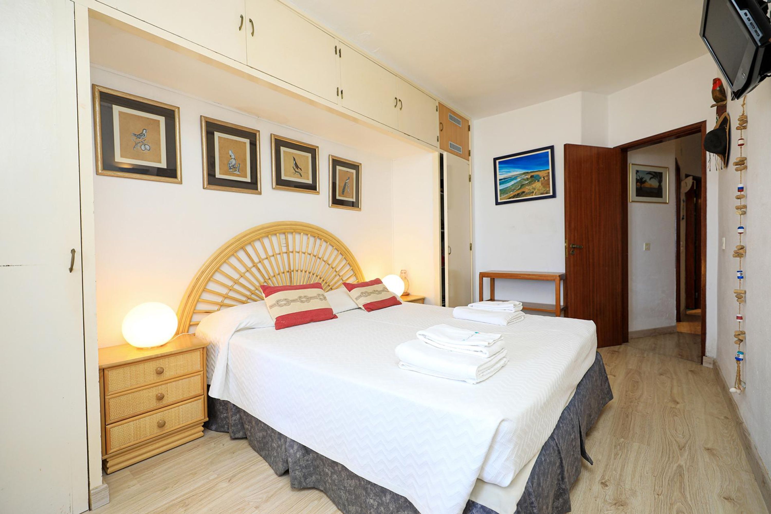 A neatly made bed with a wooden headboard, a bedside table with a lamp, and a wall with framed pictures.