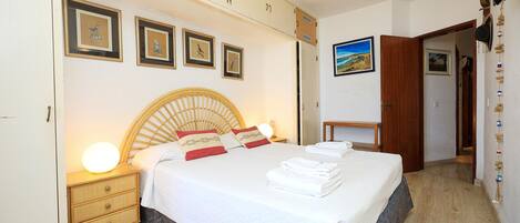A neatly made bed with a wooden headboard, a bedside table with a lamp, and a wall with framed pictures.