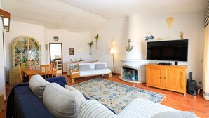 Una sala de estar con sofá, chimenea, televisión y comedor con mesa y sillas.