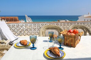 A table set with croissants, a basket of fruits, and blue glassware on a terrace overlooking the sea. - C22 - Beco do Po o Beach Townhouse in Praia da Luz (Lagos)