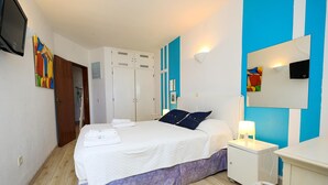 Un dormitorio con cama, una mesita de noche con lámpara, un armario y un televisor en la pared.