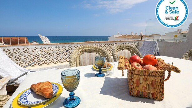 Una mesa dispuesta con un croissant, fruta y cristalería, con vistas al mar.
