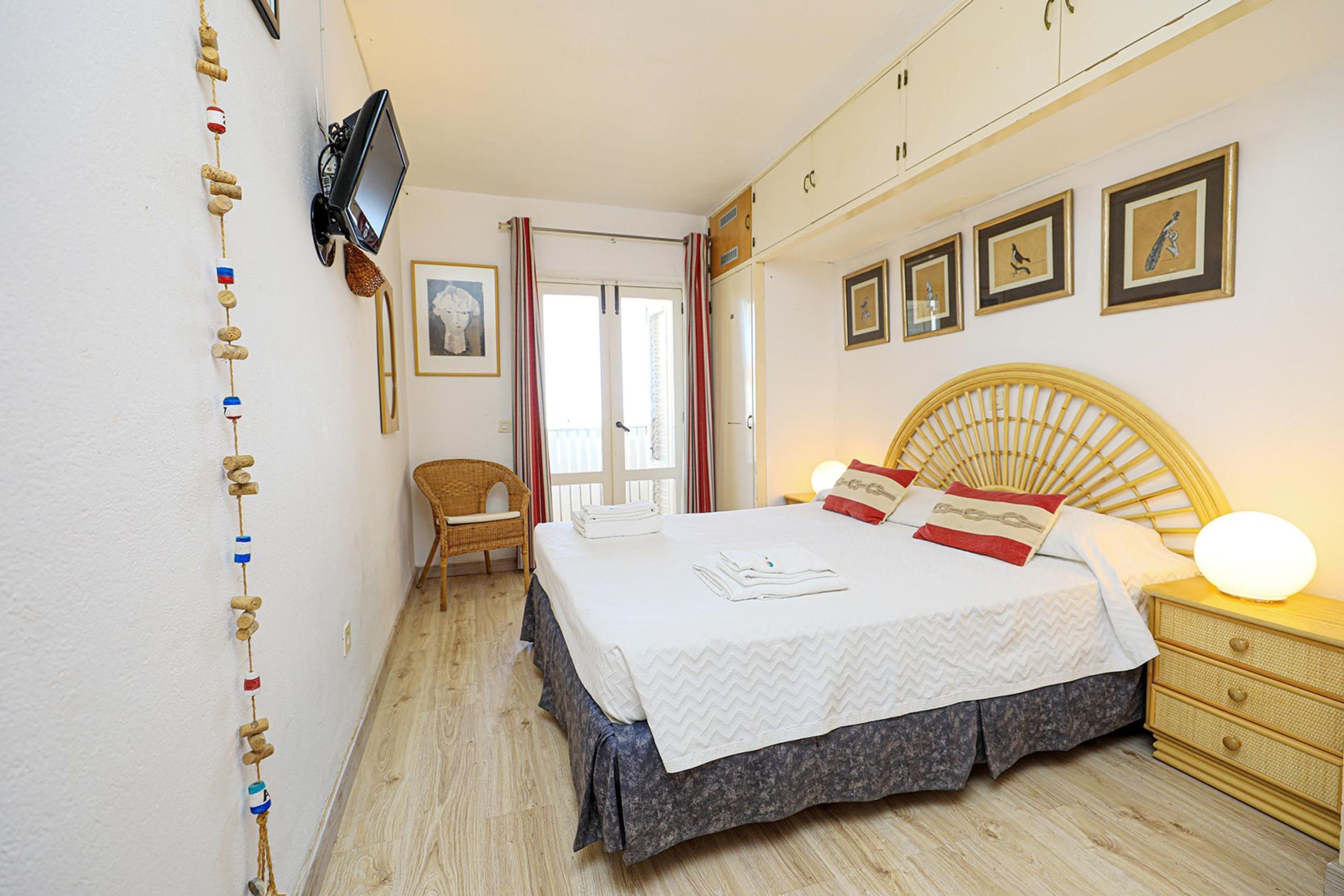 Un dormitorio con cama, mesita de noche, lámpara y televisor montado en la pared.