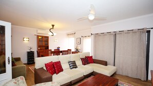A living room with a sofa, coffee table, and a dining area in the background.