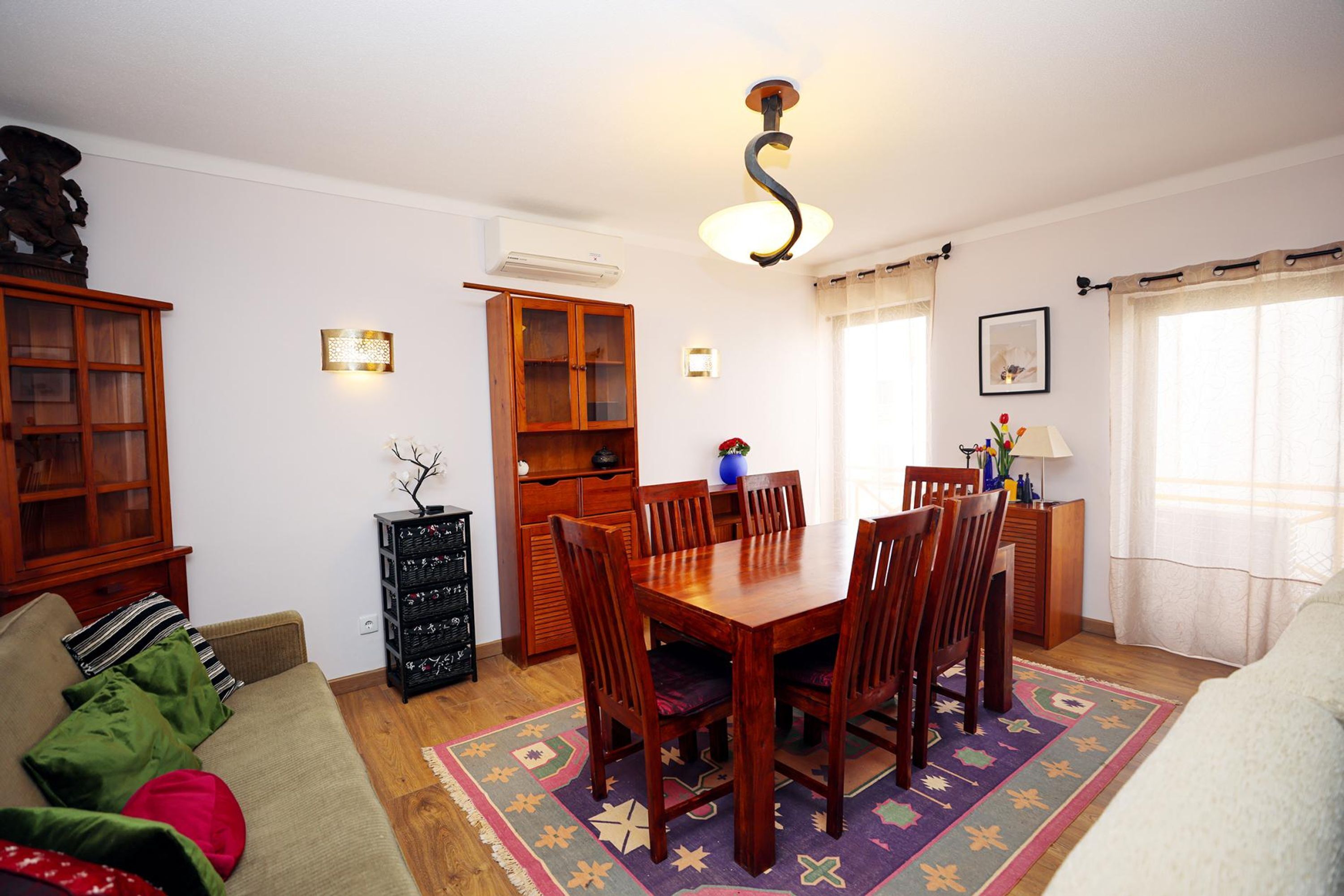 Un salon comprenant une table à manger en bois, des chaises, un canapé et un tapis à motifs.