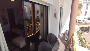 A balcony with a sofa and two chairs, a glass door leading to an interior room, and a view of a building with balconies.