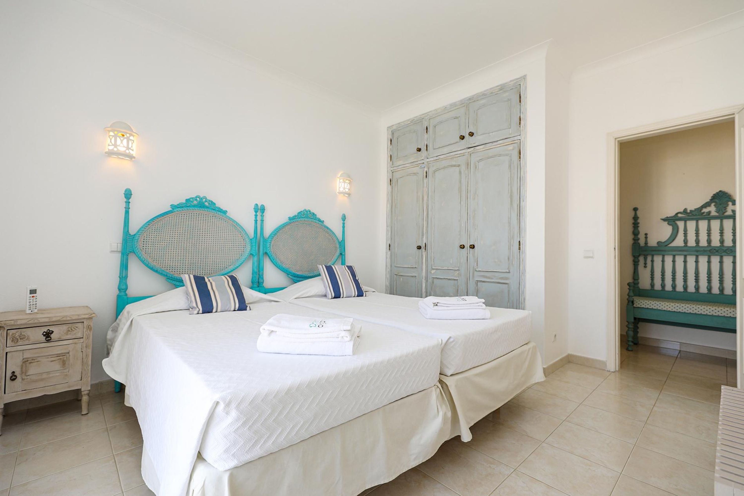 A bedroom with two beds, a nightstand, and a wardrobe.