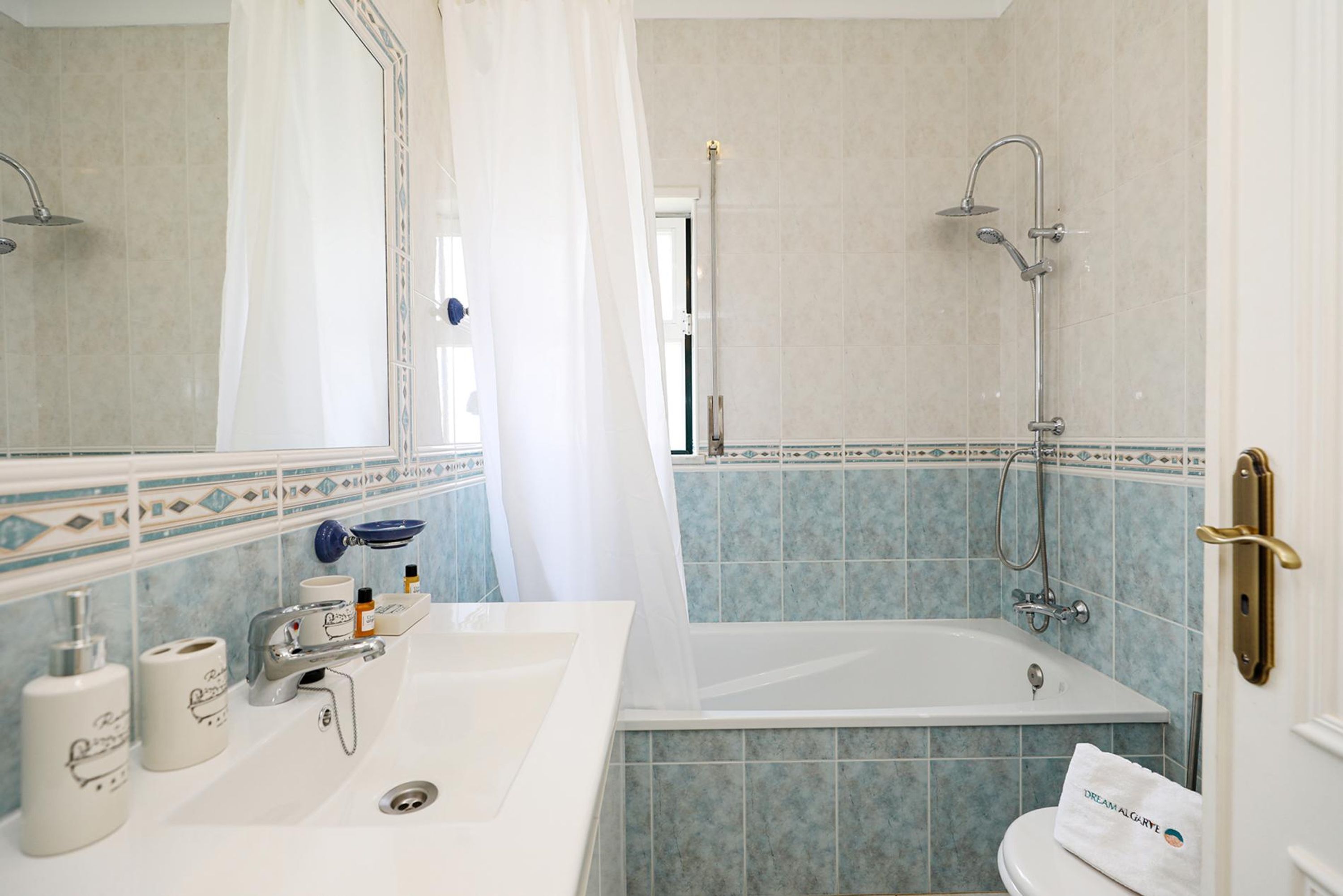A bathroom with a white sink, a bathtub, and a shower. There are toiletries on the sink, and a towel is hanging on the door.
