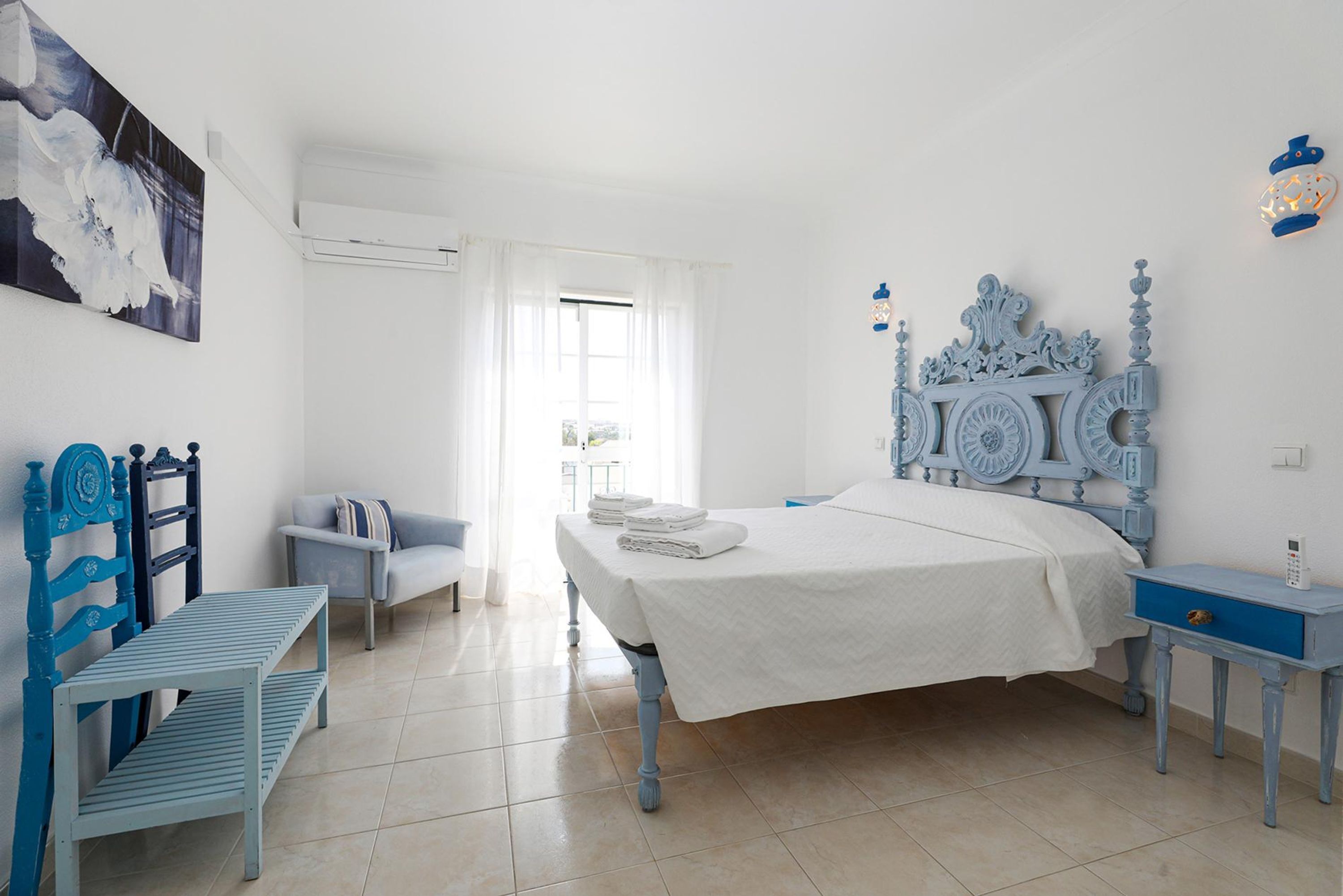 Un dormitorio con cama, banca, silla y mesita de noche.
