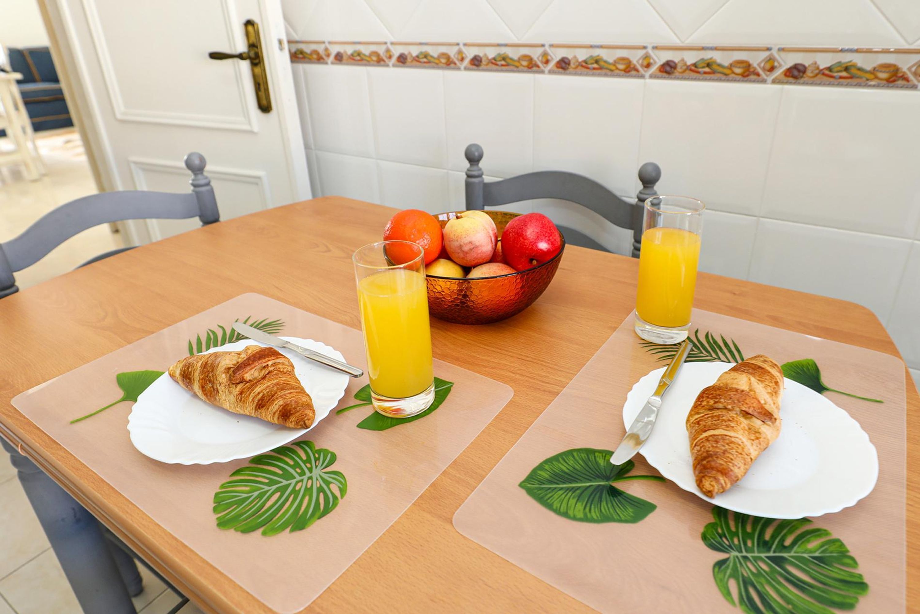 A breakfast table with two croissants, a glass of orange juice, and a bowl of fruit.