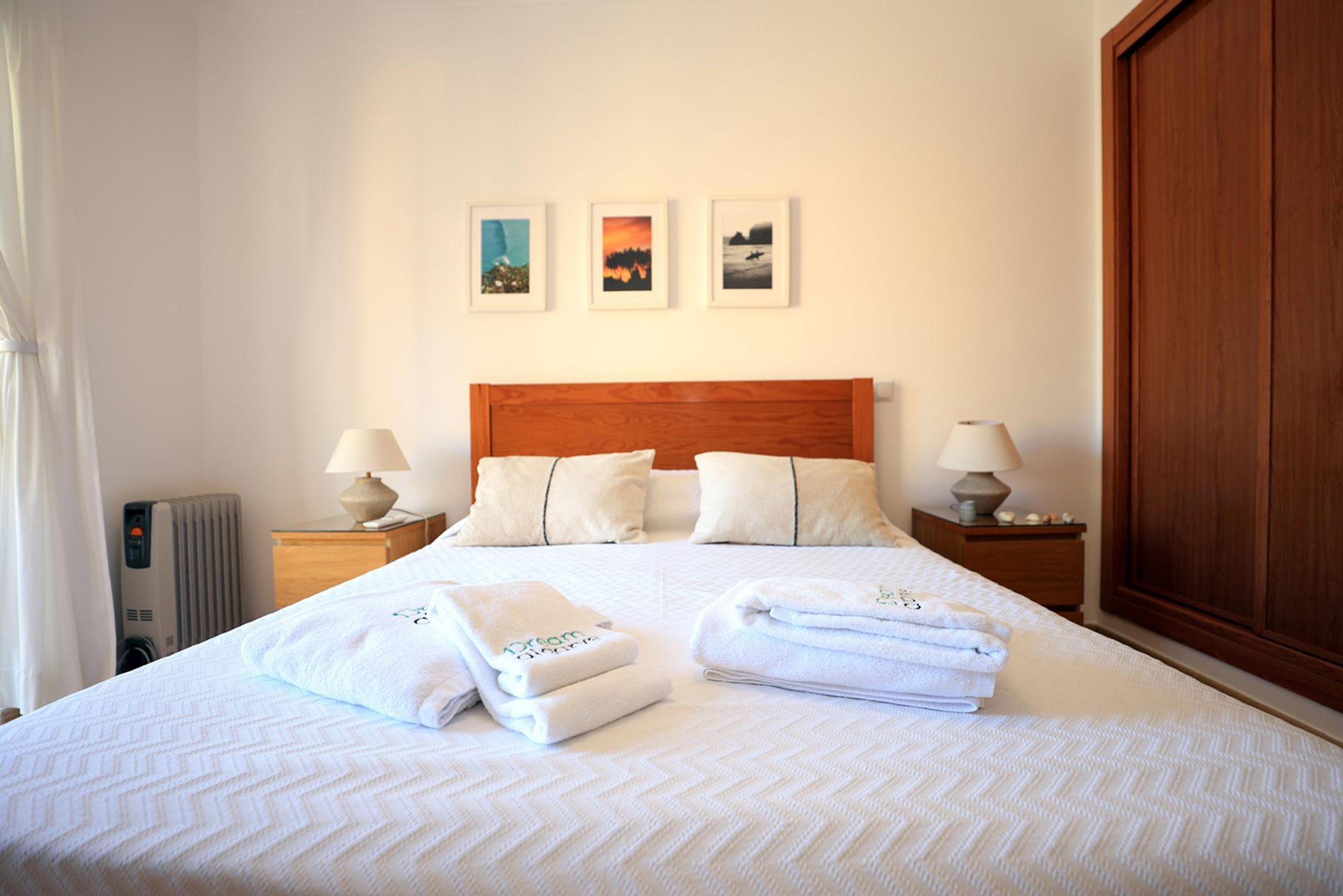 A neatly made bed with white linens and towels, a wooden headboard, and three framed pictures on the wall.