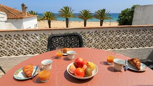 A breakfast table with croissants, fruit, and orange juice, overlooking a beach with palm trees and the sea. - B86 - Beachline Apartment in Praia da Luz (Lagos)