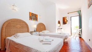 A hotel room with two beds, a wicker headboard, a painting, a Buddha statue, and a view of the outdoors. - B86 - Beachline Apartment in Praia da Luz (Lagos)