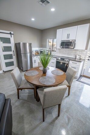 Una cocina moderna con armarios blancos, electrodomésticos de acero inoxidable y una mesa de comedor redonda con individuales.