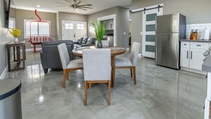 A modern kitchen with a stainless steel refrigerator, a dining area with a round table and four chairs, and a living room with a sofa and a coffee table. - 2-bedroom Home-casita , private backyard with grill, putting green,cornhole (Buckeye)