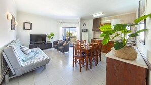 A modern living room with a sofa, TV, dining table, chairs, and a large plant. - B97 - Flor da Rocha Apartment in Portim o (Portimão)