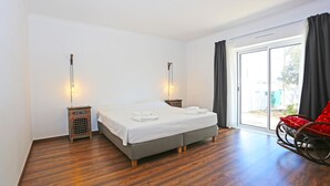 Un dormitorio con cama, dos mesitas de noche, una mecedora y un ventanal corredizo al exterior.
