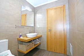 A bathroom with a wooden door, a white sink, a mirror, and a shelf with baskets.