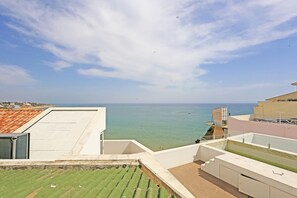 Una terraza en la azotea con vistas al mar, una piscina y un edificio con tejado de tejas.