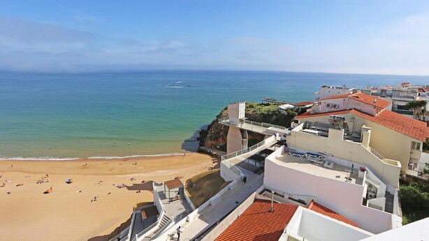 Un hotel frente al mar con vistas a la playa, múltiples balcones y cielo despejado.