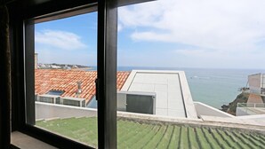 Vista desde una ventana con vistas a la costa, tejados de terracota y cielo despejado.